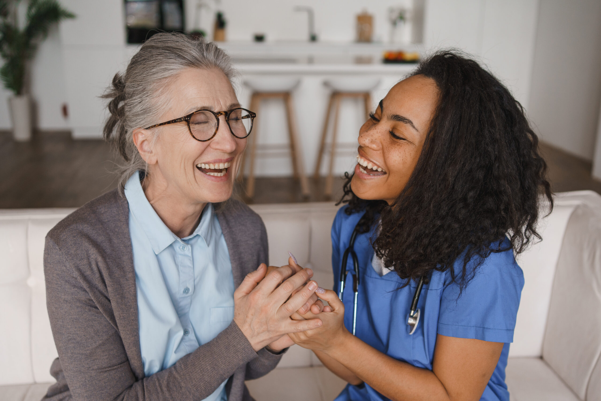 senior woman and nurse holding hands while sitting on sofa at home, elderly care, healthcare support